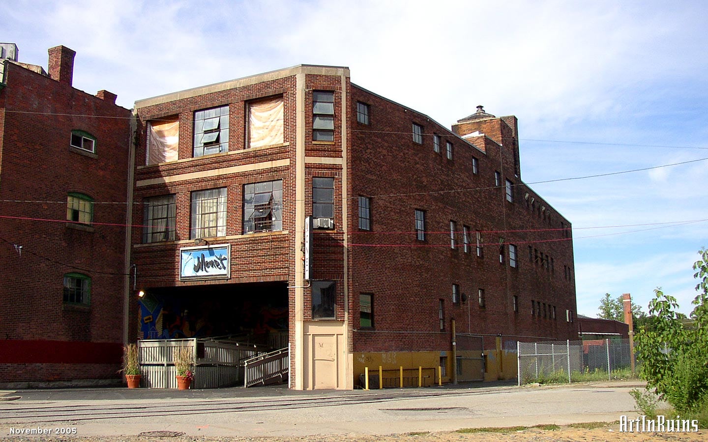 A three story red brick building with granite edging three-bays wide and four times as deep as it is wide. Built alongside a rail spur, the building bends slightly as it moves back.
