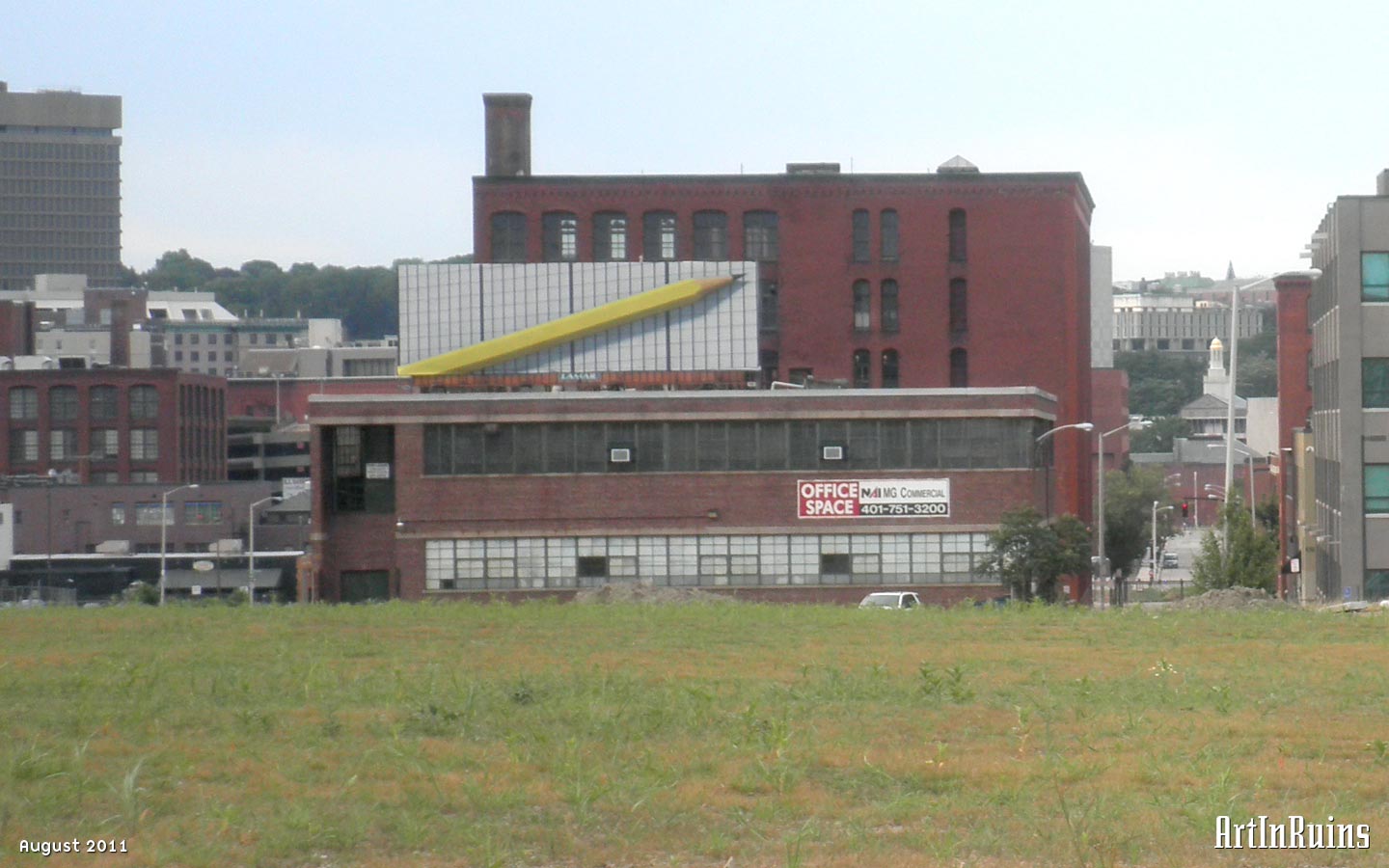 A two-story red brick industrial building on a raised basement with a cement beltcourse above each row of windows and a flat roof. The original recessed entrance is located on the southern side, two stories high and wide as a double door. A new entrance addition was added to the northwest corner. Windows are rectangular and laid edge to edge to form a continuous band around two of the building’s corners.