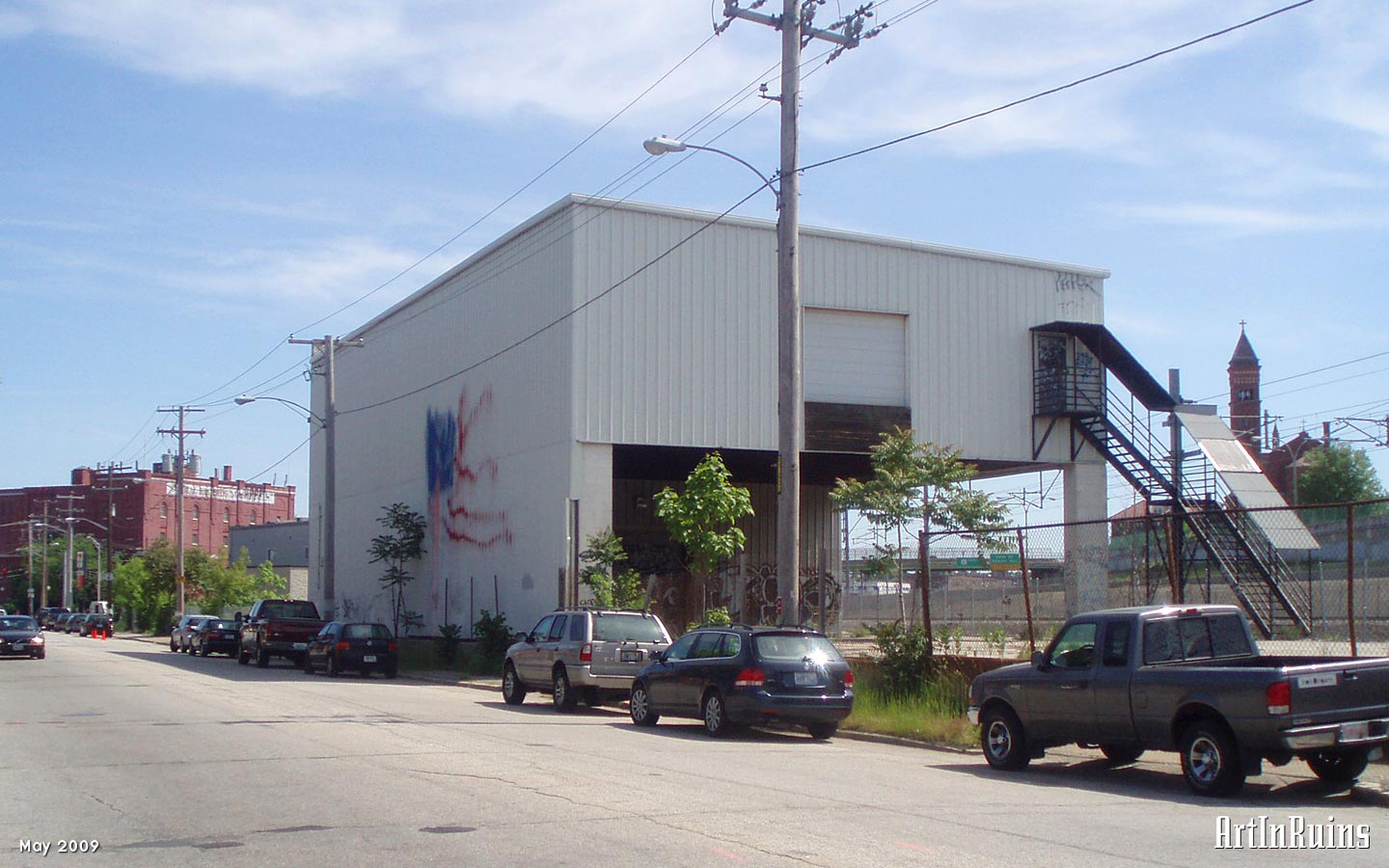 A non-descript 2-story shed along the railroad tracks used for shipping and receiving. Most of the structure is covered in corrugated steel panels and grafitti with an exterior steel stair.