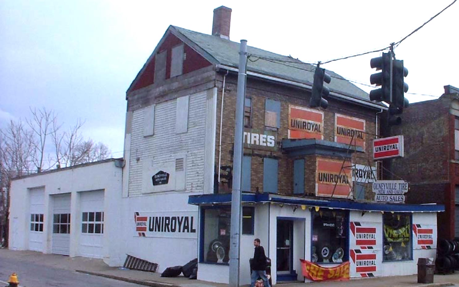 A two and a half story house with a shallow one story streetfront. For most of its life it was covered in signs for tires and tire brands Uniroyal and B.F. Goodrich.