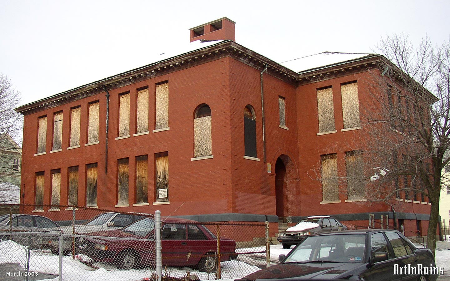 A square plan, red brick, two story former grade school building. Windows were rectangular with granite sils. Two entrances — one for boys, one for girls — are on opposite sides of the building. A cross gable shingled roof with a simple wooden cornice beneath it was on top.