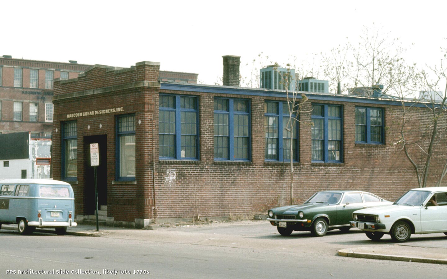 A one story red brick flat roof industrial building with a narrow façade and simple ornamentation.