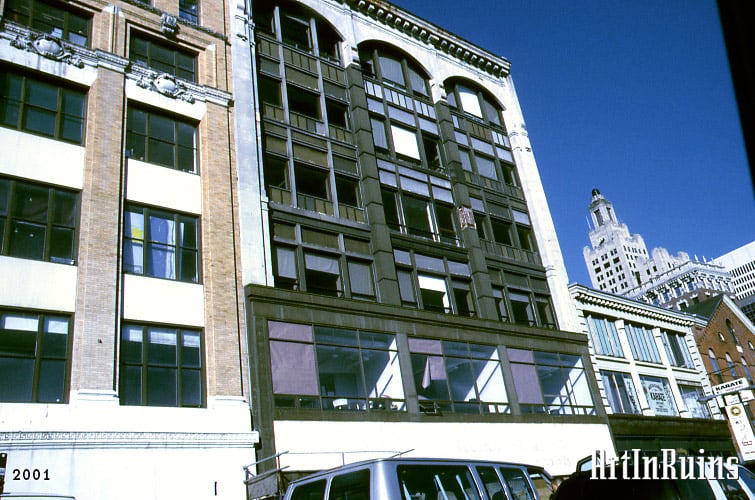 A six-story, three bay wide commercial building clad in steel and aluminum with a rectangular set of windows on the first two floors, narrower rectangular windows on the third through fifth, and rounded arched windows across the top floors